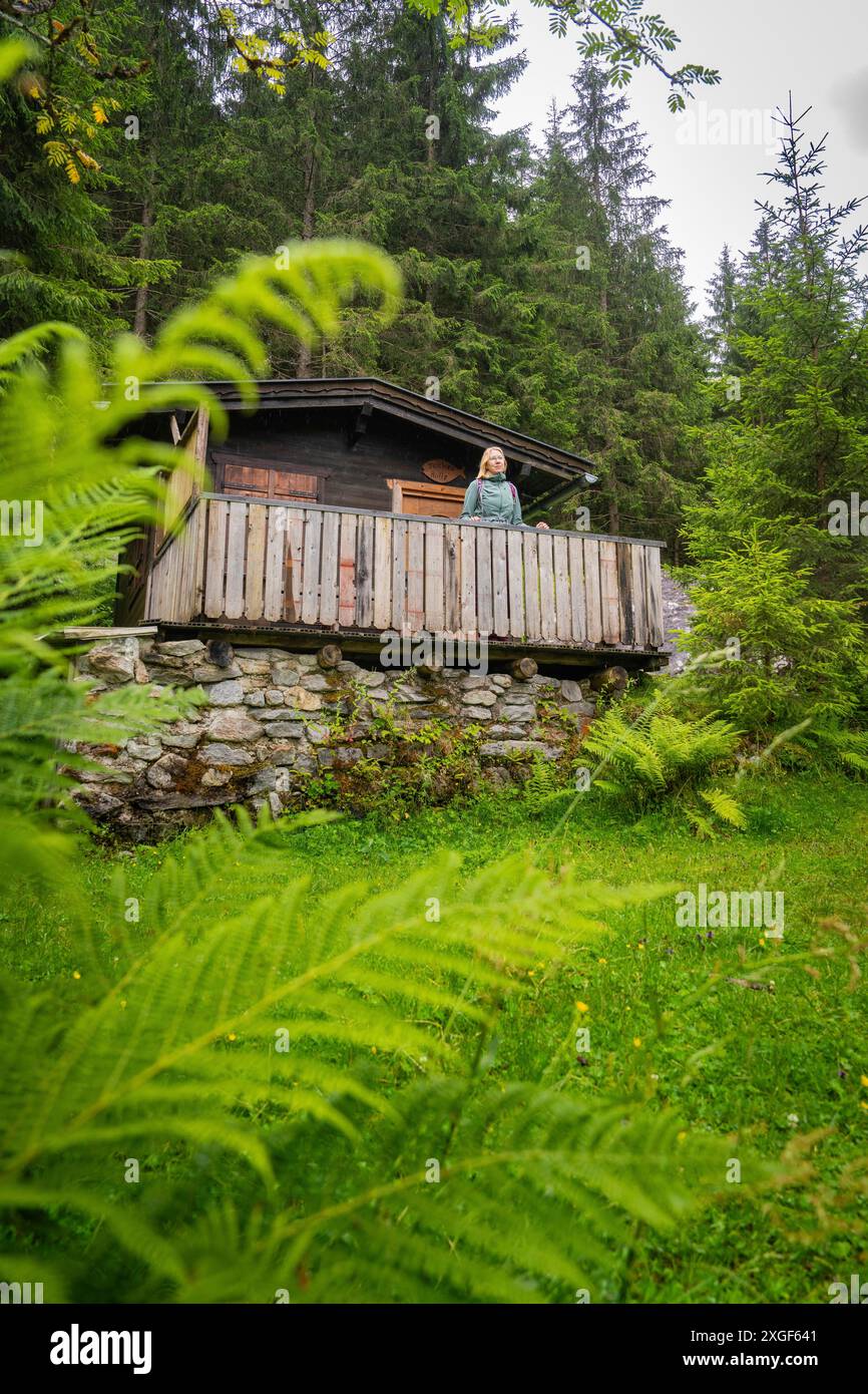 Eine Hütte im Wald, umgeben von grünen Farnen. Eine Person steht auf der Veranda und genießt die Natur, Stilluptal, Zillertal. Österreich Stockfoto