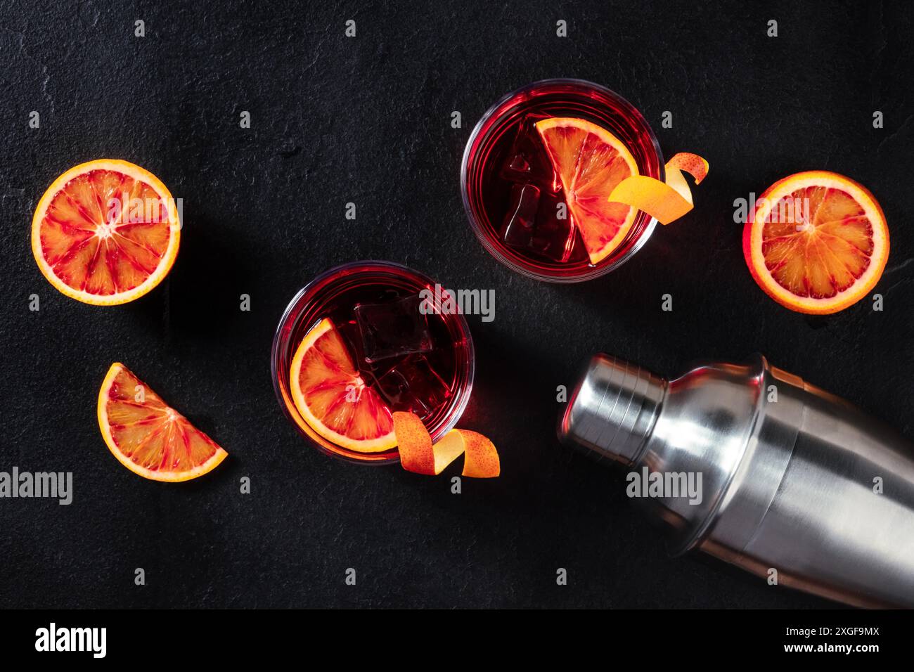 Negroni-Cocktails, ein flacher Lay-Shot mit Blutorangen und einem Shaker auf schwarzem Hintergrund Stockfoto