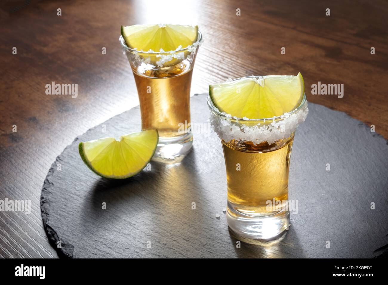 Tequila-Schüsse mit Salzrand und Limettenscheiben, serviert auf einem Tablett aus schwarzem Schiefer Stockfoto