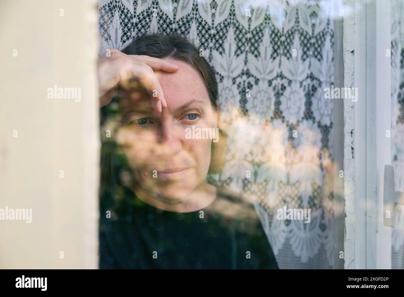 Porträt der Reifen erwachsenen kaukasischen Frau traurig und depressiv, die aus dem Fenster blickt, geistige Gesundheit und Geisteszustand Konzept, selektiver Fokus Stockfoto