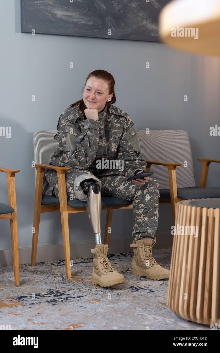 Im Wartezimmer sitzend, Frau in undefinierter Uniform mit Beinprothesen am Telefon Stockfoto