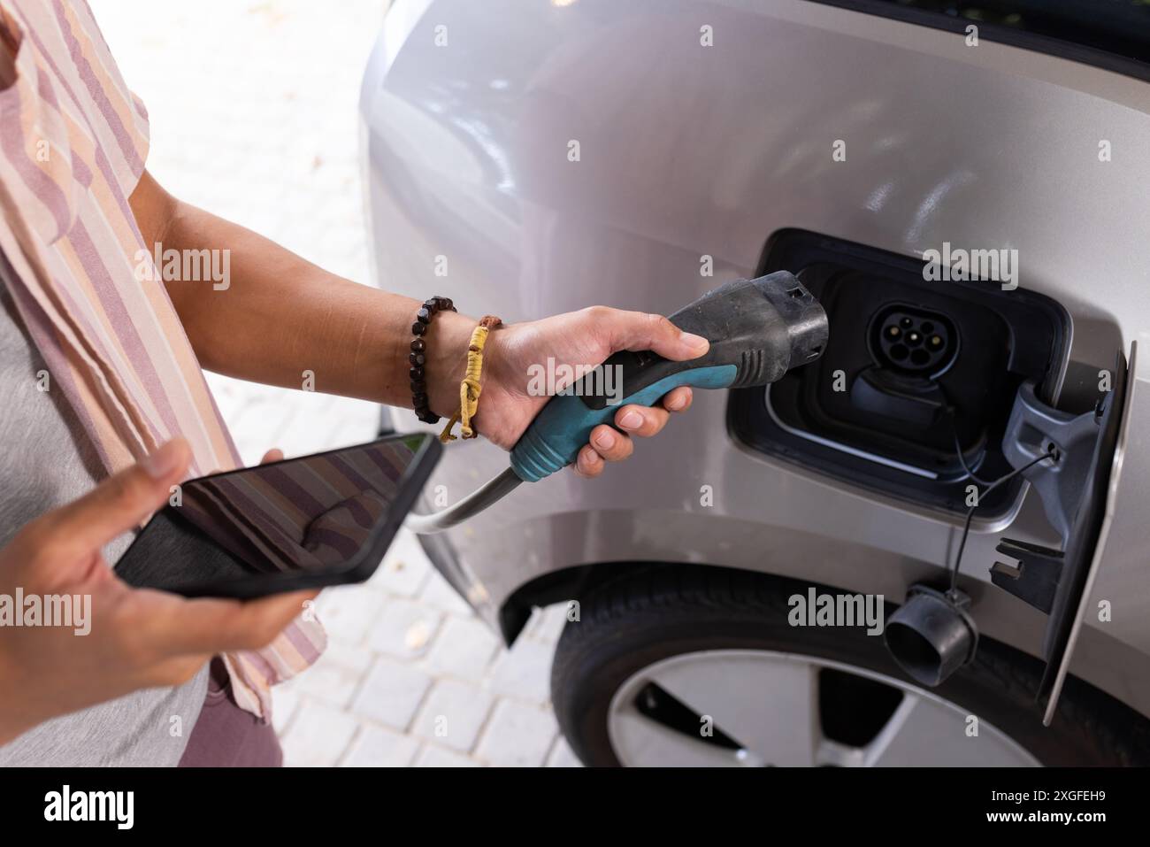 Laden eines Elektroautos, Mann hält Ladekabel und Smartphone, konzentriert sich auf die Aufgabe Stockfoto