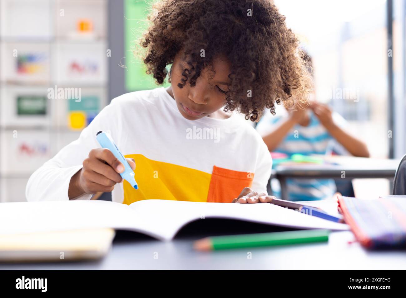 Glücklicher afroamerikanischer Schuljunge, der am Schreibtisch im Klassenzimmer sitzt Stockfoto