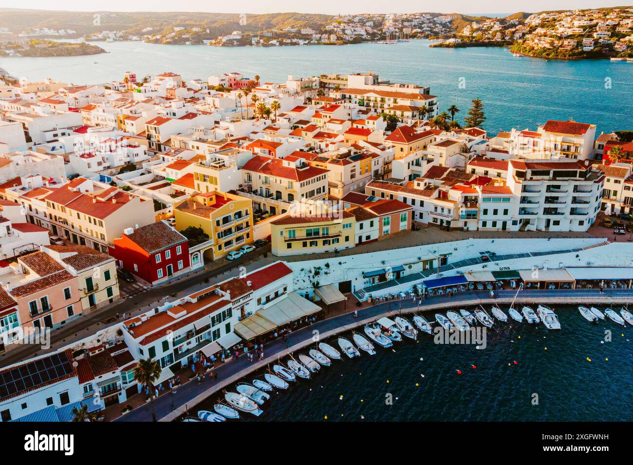 Blick aus der Vogelperspektive auf die traditionelle Stadt es Castell an der Küste Menorcas mit Hafen und Booten bei Sonnenuntergang während der Sommersaison. Malerische balearen Schlepptau Stockfoto