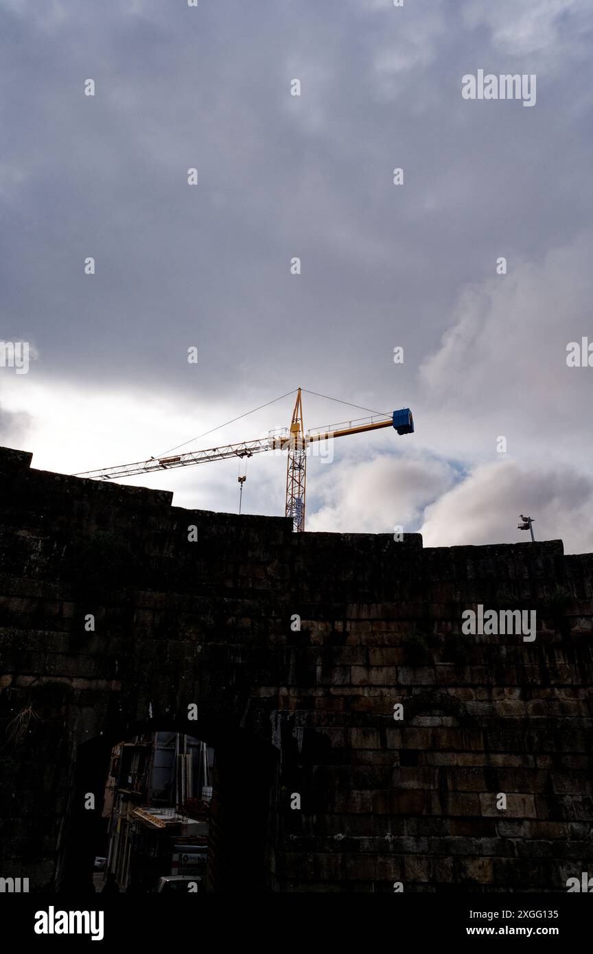 Der Baukran erhebt sich über die alten Steinmauern in Porto und verbindet die historische Vergangenheit der Stadt mit der laufenden Entwicklung Stockfoto