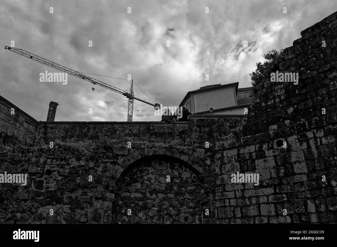 Der Baukran erhebt sich über die alten Steinmauern in Porto und verbindet die historische Vergangenheit der Stadt mit der laufenden Entwicklung Stockfoto