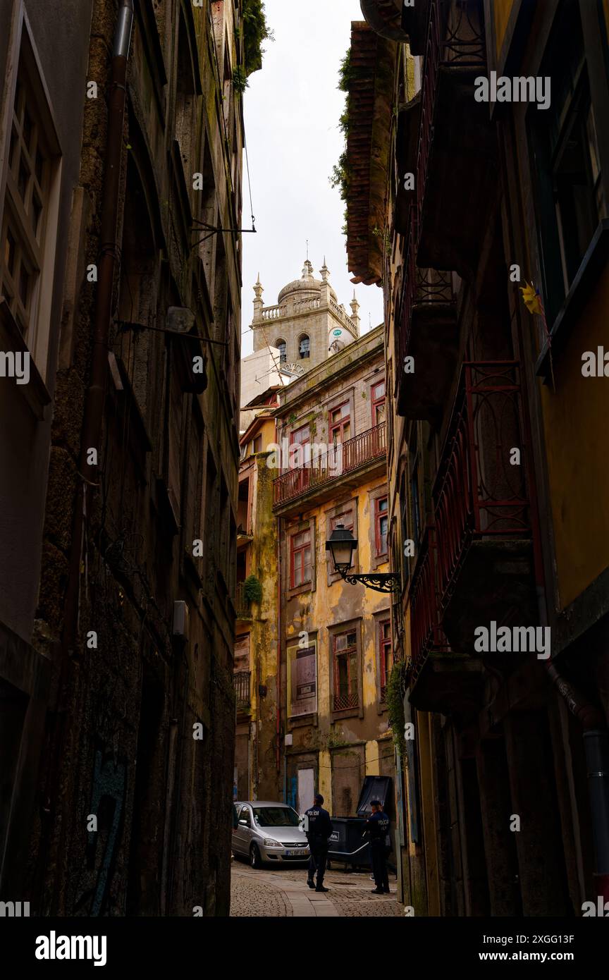 Die enge, schattige Gasse in Porto zeigt die komplizierten Details historischer Gebäude, die zu einem Paar Polizisten und einem Kirchturm führen Stockfoto