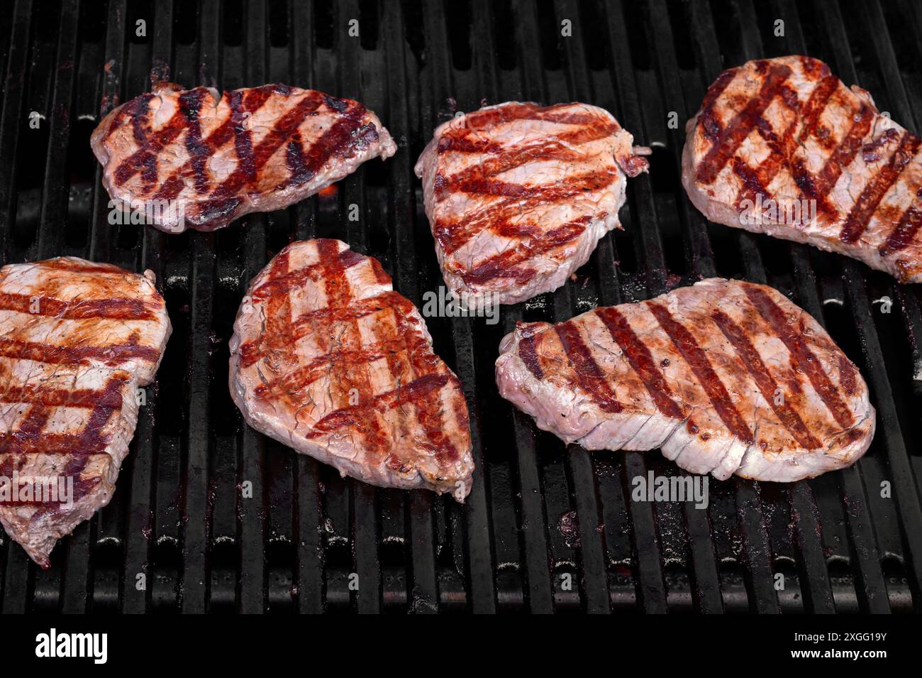 Mehrere gut gewürzte Steaks, die perfekt auf einem feurigen Grill kochen Stockfoto