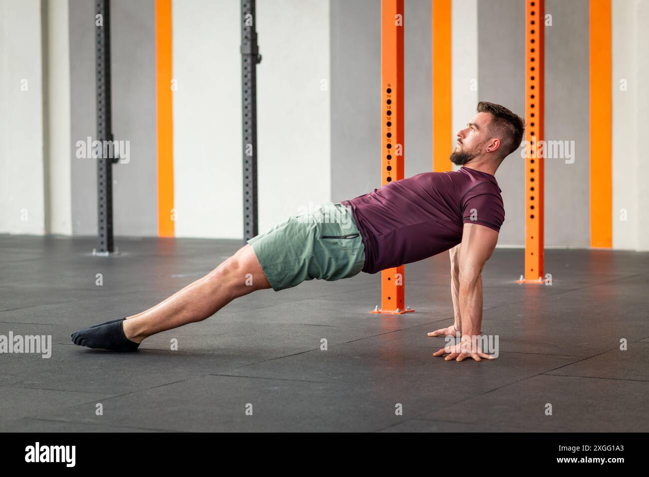 Seitenansicht eines fokussierten Mannes, der im modernen Fitnesscenter Calisthenics-Reverse Plank-Übungen auf dem Boden durchführt Stockfoto