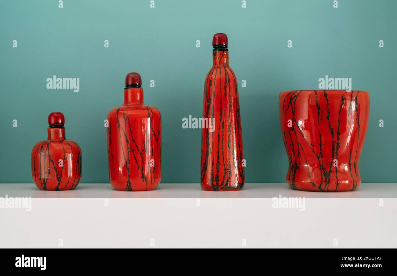 Vier rote Muranoglas mit schwarzen Streifen stehen auf dem weißen Regal Stockfoto