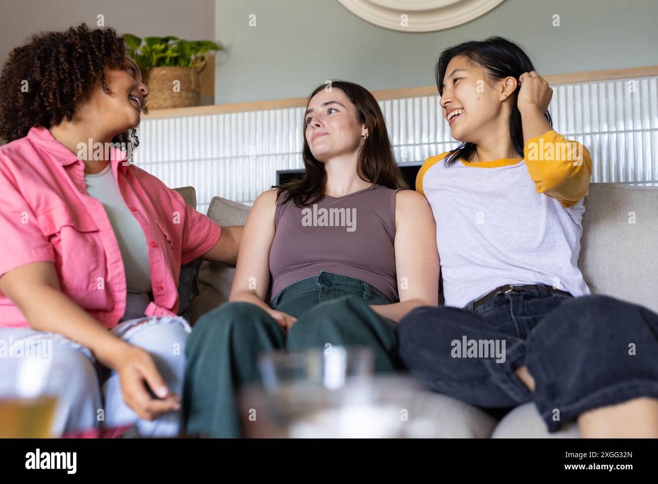 Auf der Couch sitzend, drei Freundinnen reden und lachen zu Hause zusammen Stockfoto