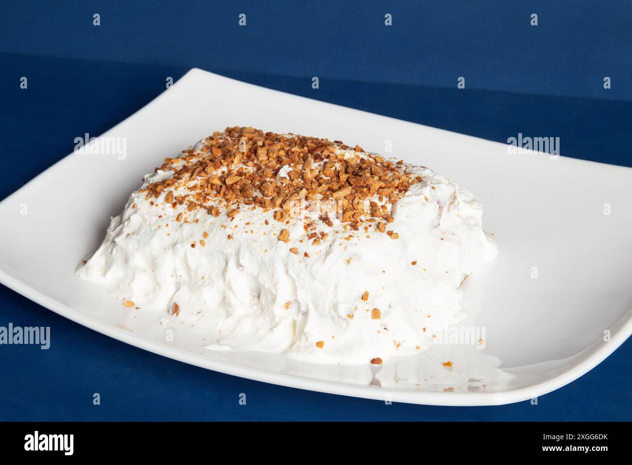 Ein köstlicher süßer Leckerbissen besteht aus einem cremigen, gepeitschten Topping, das großzügig mit knusprigen Mandelstücken auf einer weißen Platte gegen eine tiefblaue Ba bestreut ist Stockfoto