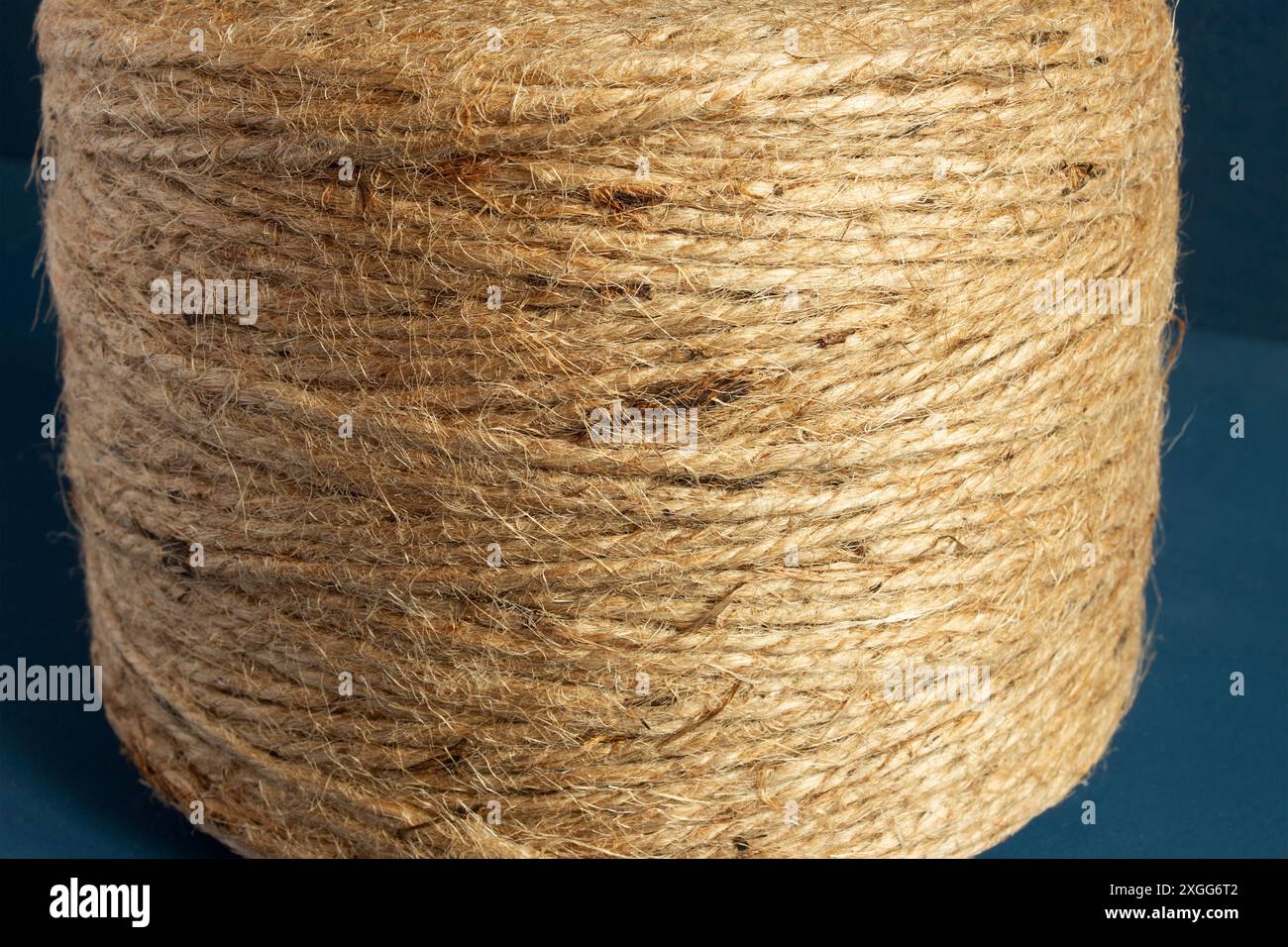 Die Nahaufnahme einer Spule aus Naturfaser-Garn vor einem dunkelblauen Hintergrund unterstreicht die komplizierte Struktur und das Muster des Garns. PVerpackung, Rost Stockfoto