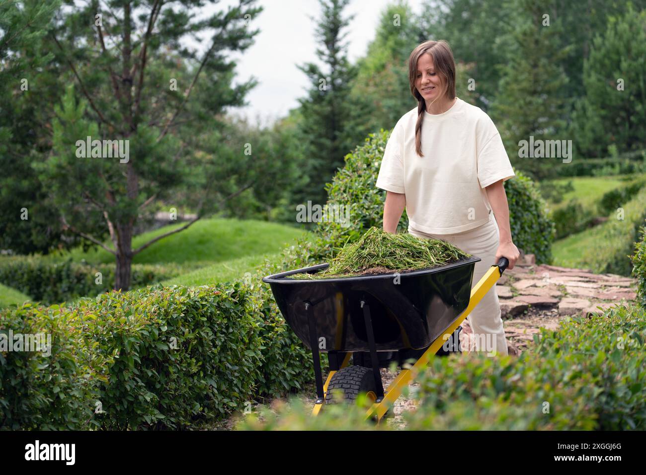 Eine Frau gärtet in einem üppigen Garten mit Schubkarre, was Wohlbefinden und Naturverbundenheit fördert Stockfoto