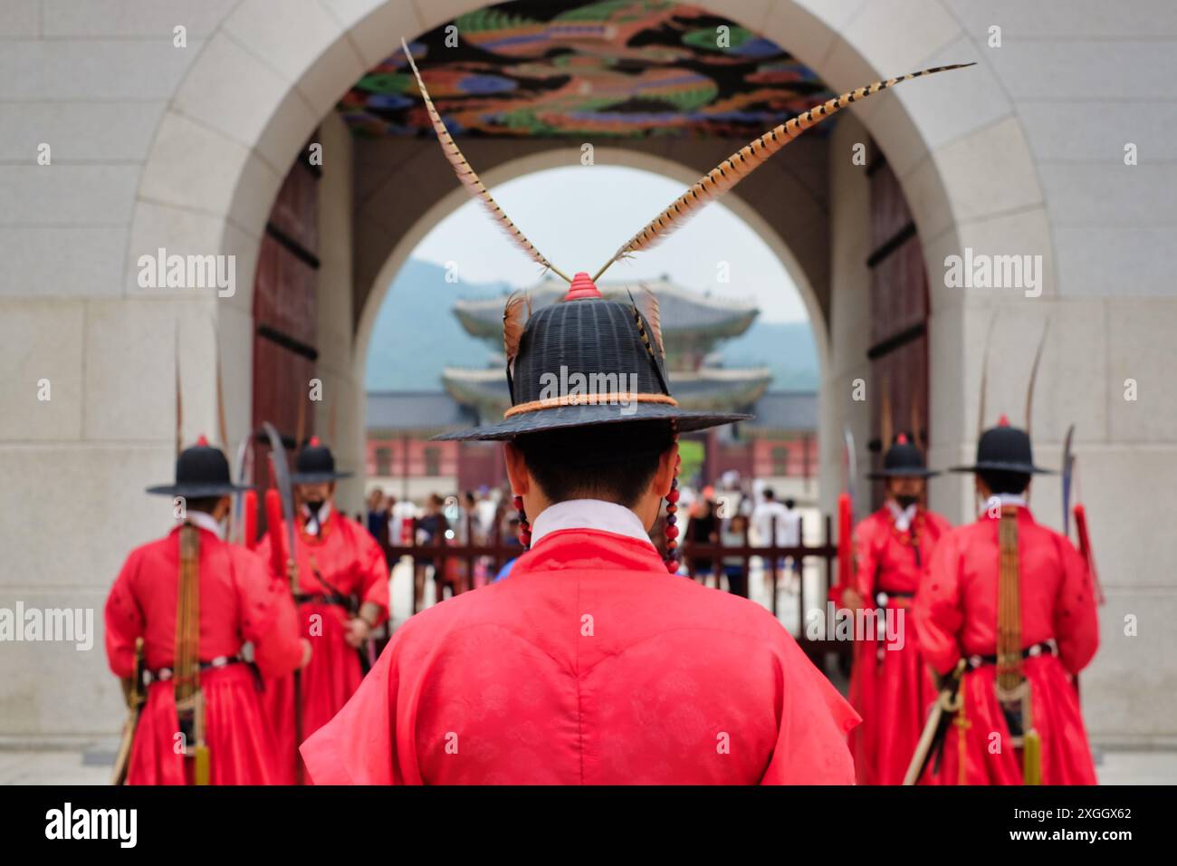 Koreanische Palastwächter in traditionellen roten Uniformen und kunstvollen Hüten stehen unter einem bogenförmigen Tor auf der Spur Stockfoto