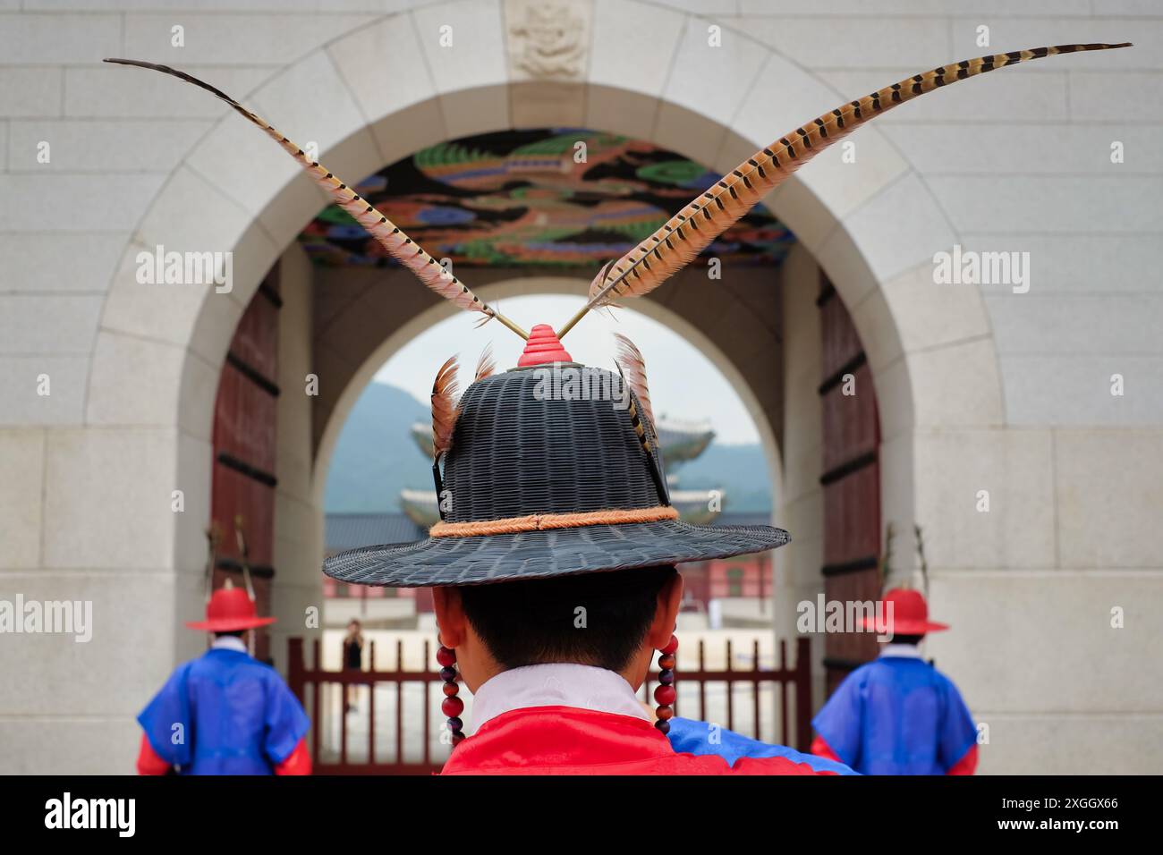 Koreanischer Palastwächter in traditionellem Hut mit Federn, eingerahmt von einem Bogen mit verziertem Dach Stockfoto