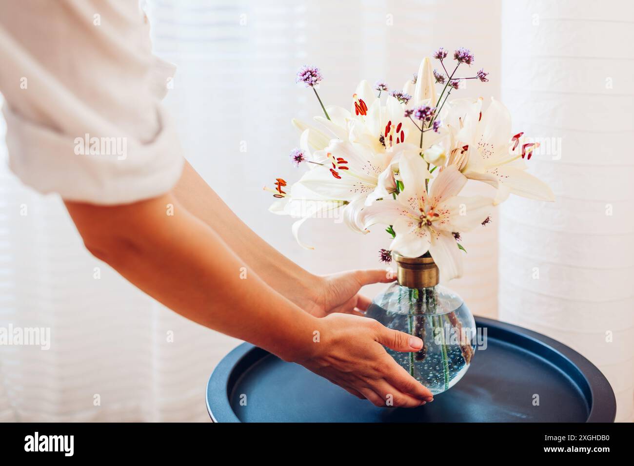 Frau legt Blumenstrauß in Vase auf Couchtisch zu Hause. Lieferung von frischen Blumenarrangements der Saison für die Inneneinrichtung Stockfoto