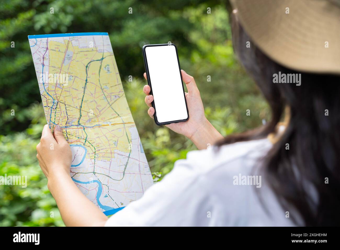 Nahaufnahme von Frauenhänden mit Smartphone und Karte im Waldhintergrund, Bildschirm isolieren. Glückliche junge Frau mit einer Karte, Smartphone auf nat Stockfoto