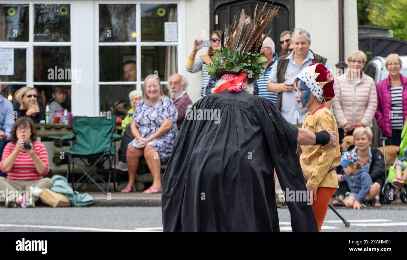 Die Rendham Mummers feiern die Sommersonnenwende in traditioneller Gesichtsfarbe, 2018 und die Straße vor dem White Horse Pub mit vorbeifahrendem Verkehr. Stockfoto