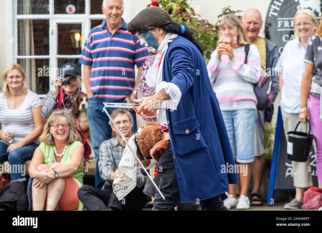 Die Rendham Mummers feiern die Sommersonnenwende in traditioneller Gesichtsfarbe, 2018 und die Straße vor dem White Horse Pub mit vorbeifahrendem Verkehr. Stockfoto