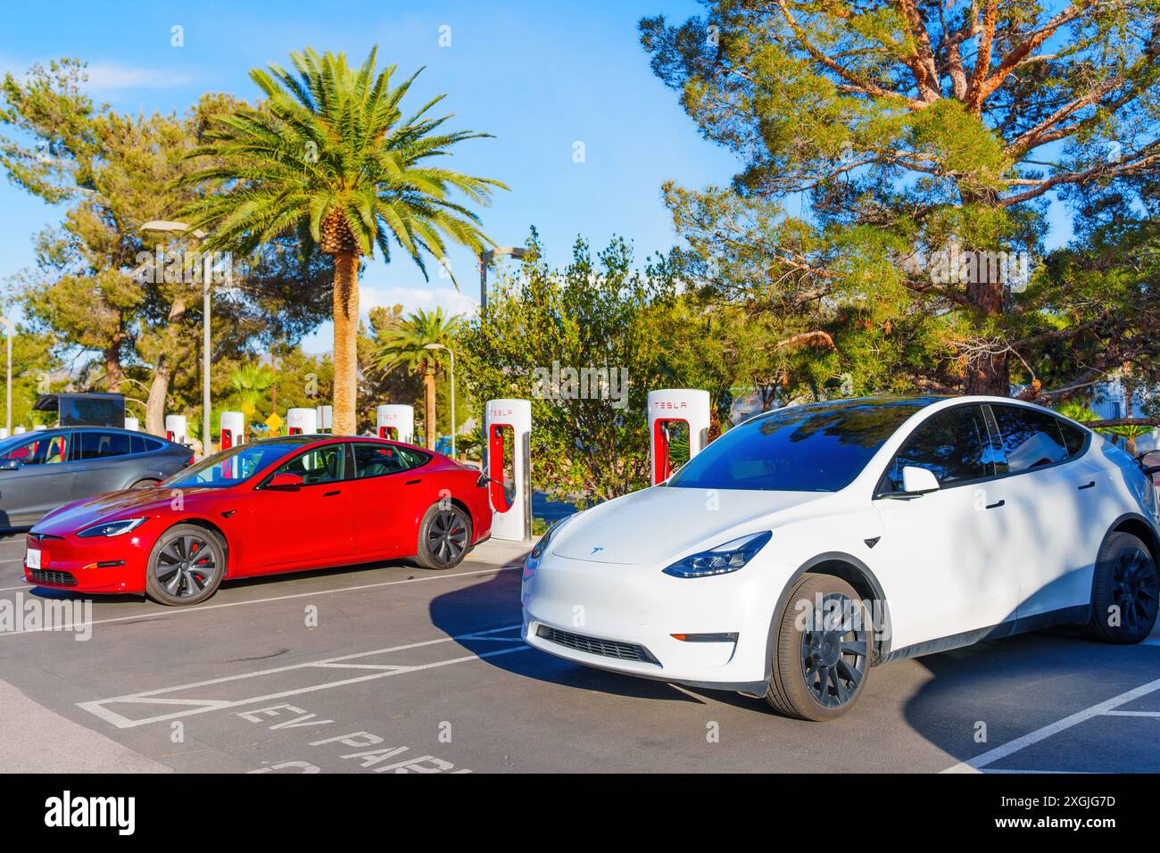 Los Angeles, Kalifornien - 15. April 2024: Zwei Elektroautos, darunter rote und weiße Tesla-Modelle, laden an der Tesla Supercharger Station auf einem klaren s auf Stockfoto