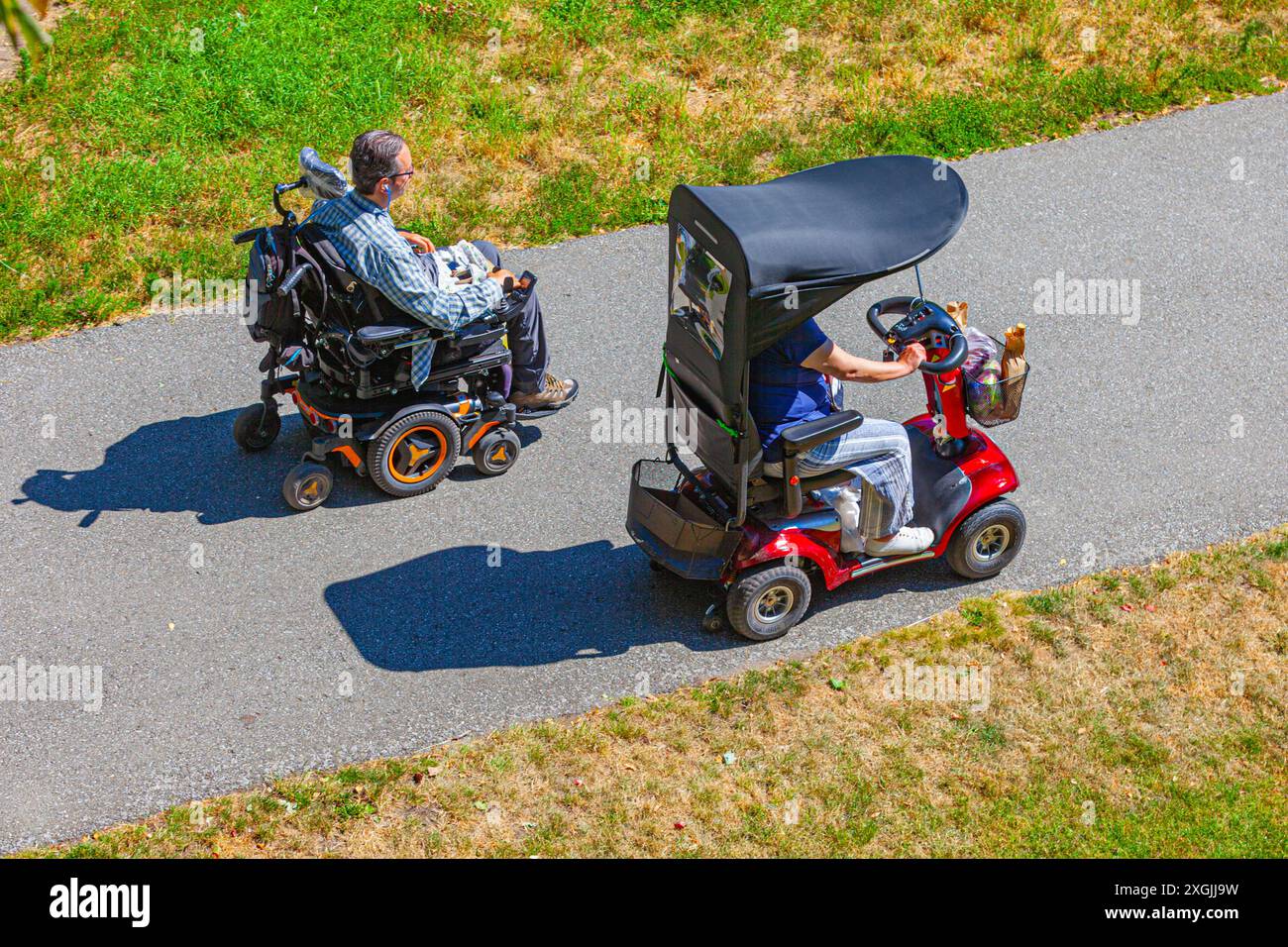 Körperbehinderte Menschen, die mit ihren motorisierten Rollern auf einem Fußweg fahren Stockfoto
