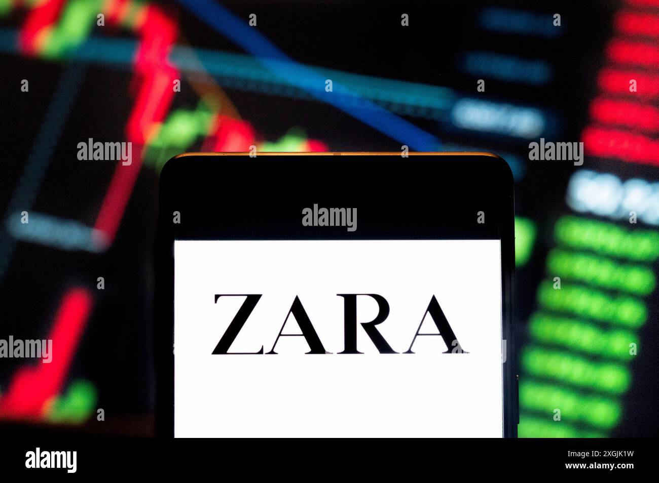 In dieser Fotoabbildung zeigt das spanische multinationale Bekleidungsdesign-Einzelhandelsunternehmen von Inditex (BME: ITX), Zara, Logo auf einem Smartphone mit einem wirtschaftlichen Börsenindex-Diagramm im Hintergrund. Stockfoto