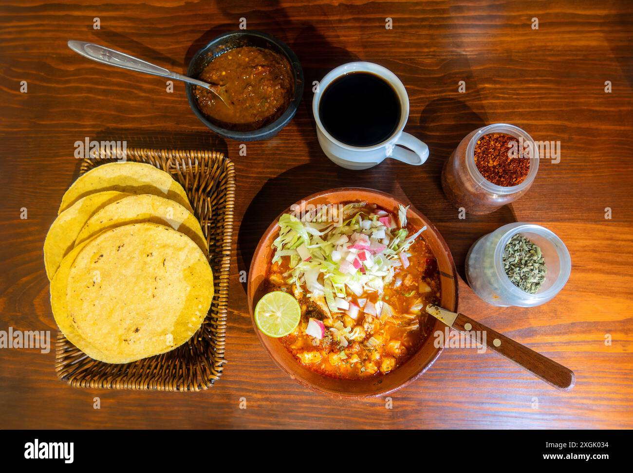 Genießen Sie den Geschmack von authentischem mexikanischem roten Pozole, wunderschön präsentiert mit Rettich, Salat, Hominy und zartem Schweinefleisch. Gepaart mit einer Tasse Kaffee, spi Stockfoto
