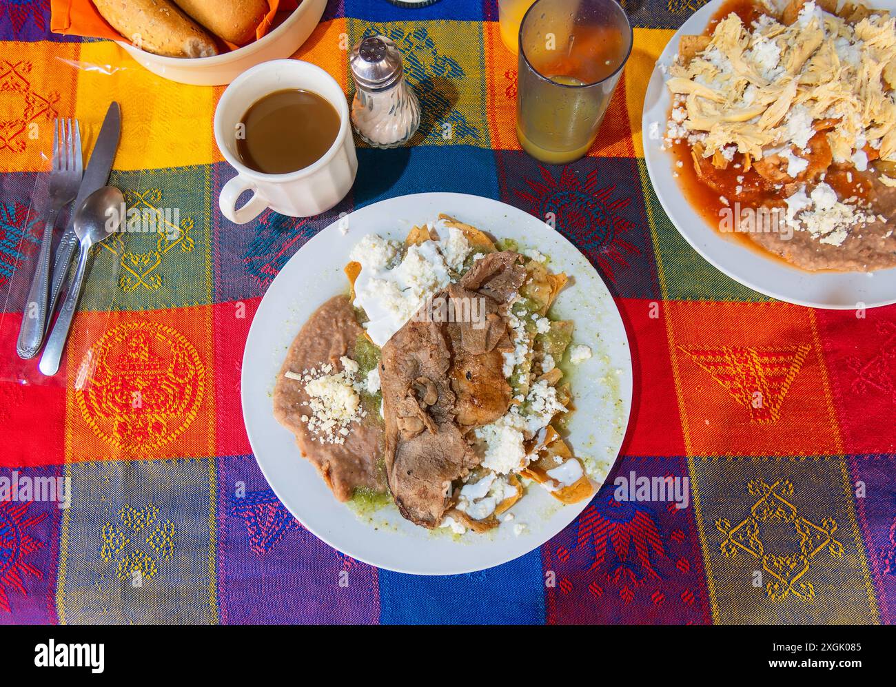 Authentisches mexikanisches Frühstück mit Chilaquiles mit zartem Fleisch, frischen Bohnen und frischem Käse, serviert mit einer Tasse dampfendem Kaffee. Vibra Stockfoto
