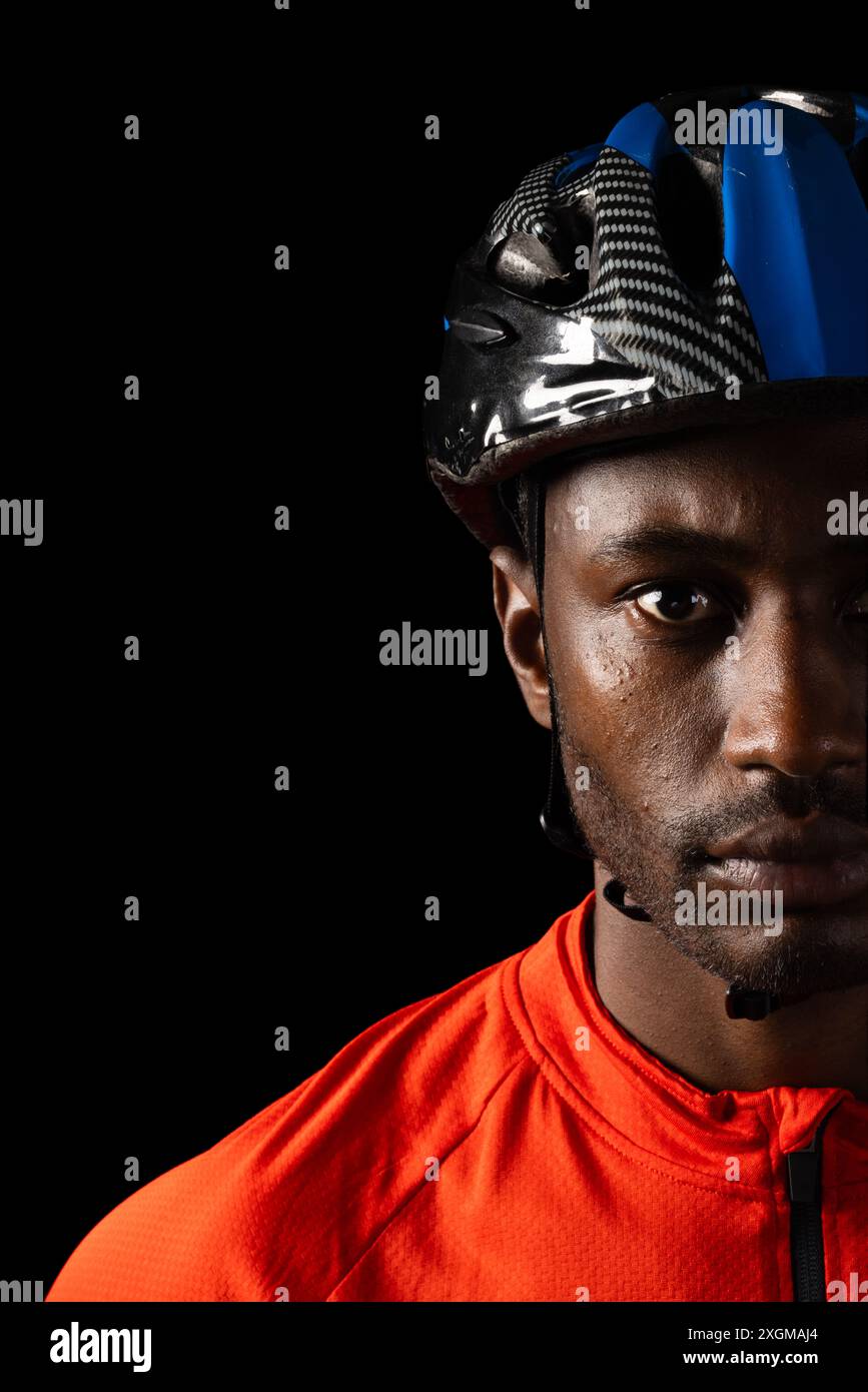 Fokussierter afroamerikanischer Radfahrer mit Helm, Kopierraum auf schwarzem Hintergrund. Sein intensiver Blick deutet auf Entschlossenheit und Bereitschaft für Co. Hin Stockfoto