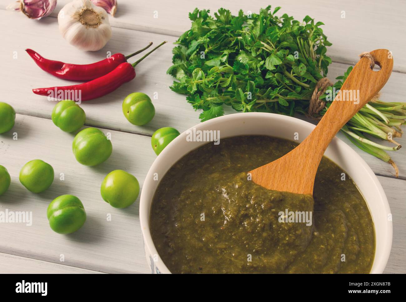 Tkemali-Sauce, traditionelle georgische Küche, grüne Kirschpflaume, mit Zutaten für Soße, Koriander, Pfeffer, Knoblauch, auf einem weißen Holz Stockfoto