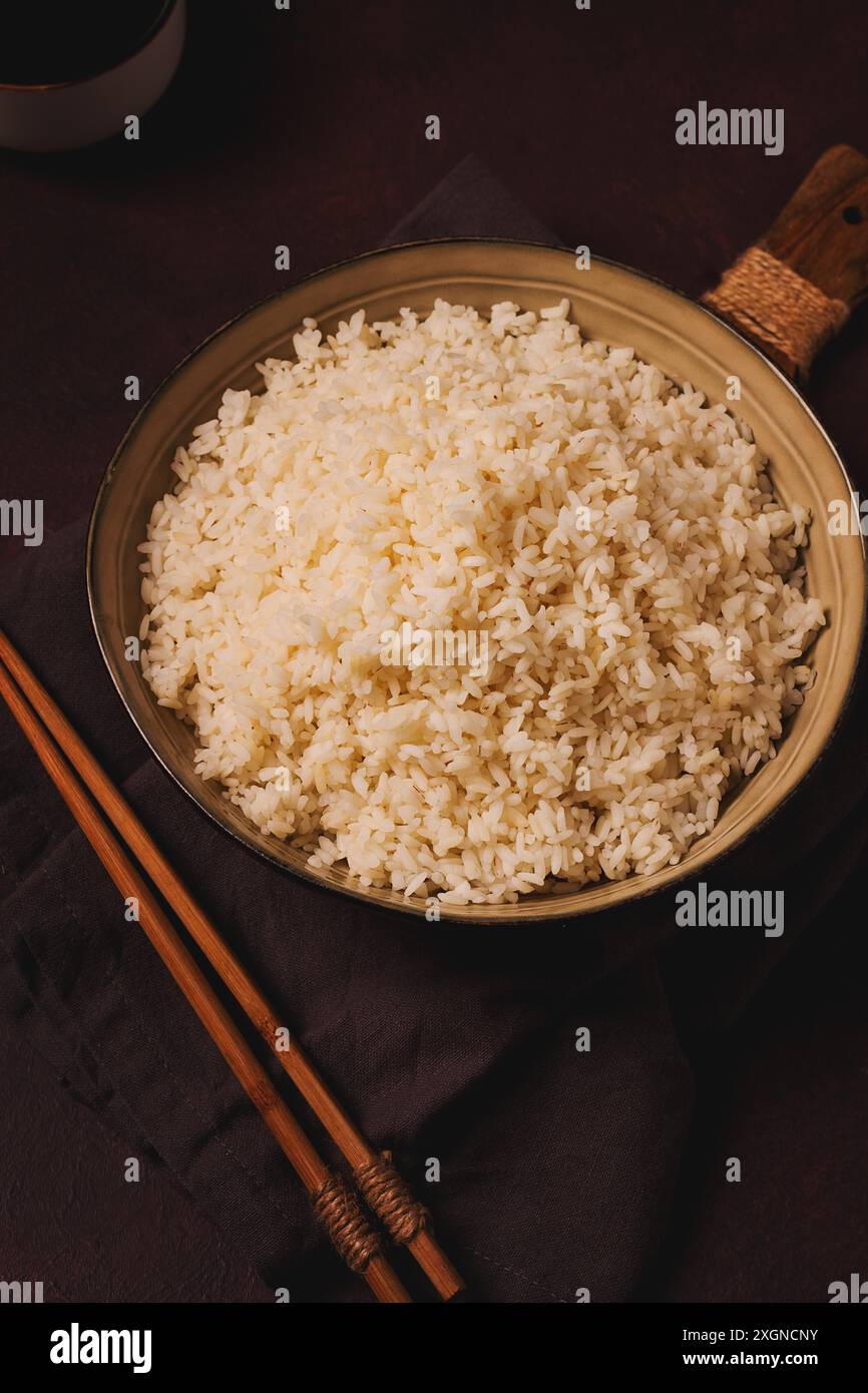Ein Teller mit gekochtem Reis, mit Holzstöcken, auf braunem Hintergrund, keine Leute, selektiv fokussiert, getönt Stockfoto