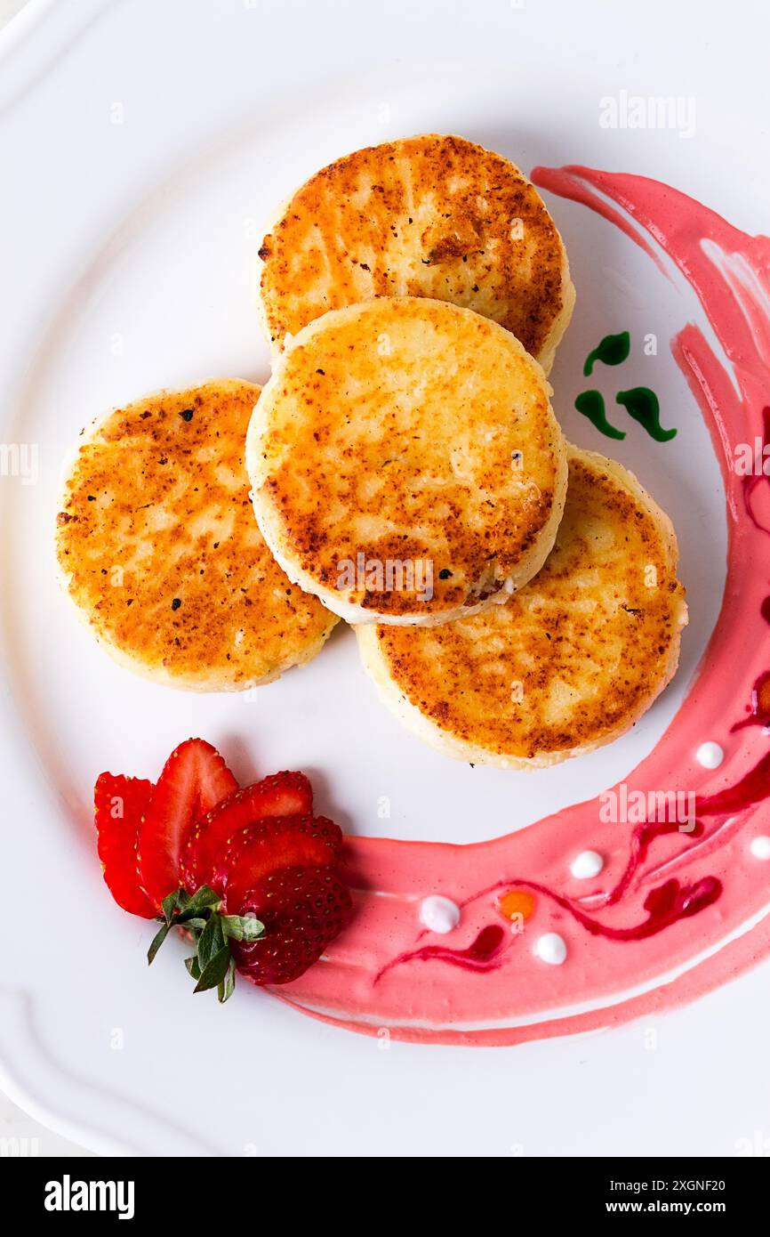 Hüttenkäsepfannkuchen, auf einem weißen Teller dekoriert mit Soße, frische Erdbeere, Nahaufnahme, keine Leute Stockfoto