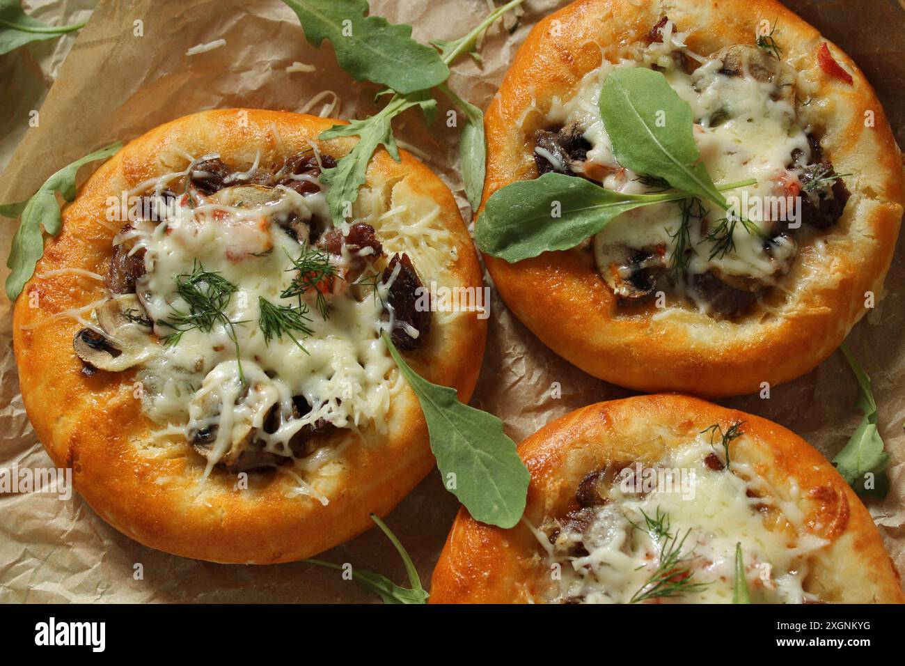 Drei Mini-Pizzen mit Pilzen, geschmolzenem Käse, garniert mit Rucola auf Pergamentpapier Stockfoto