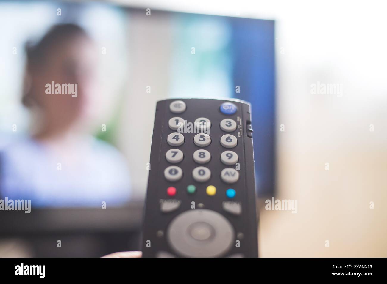 Halten Sie eine Fernbedienung in der Hand, Vordergrund, fernseher im unscharfen Hintergrund. Streaming Stockfoto