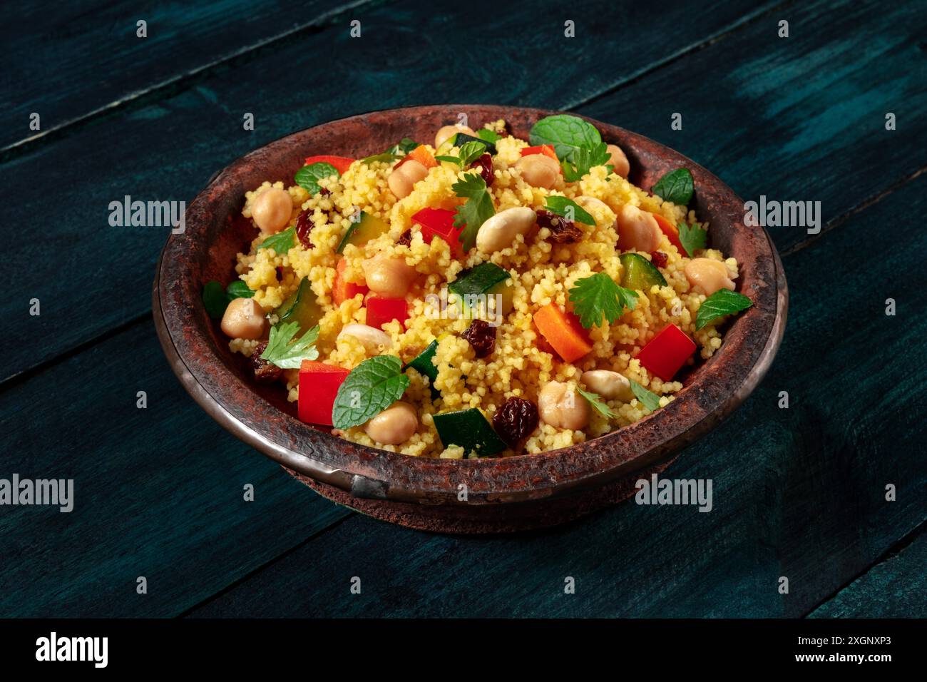 Couscous im traditionellen Tagine, mit Gemüse und Kräutern, auf einem dunklen rustikalen Holzhintergrund Stockfoto