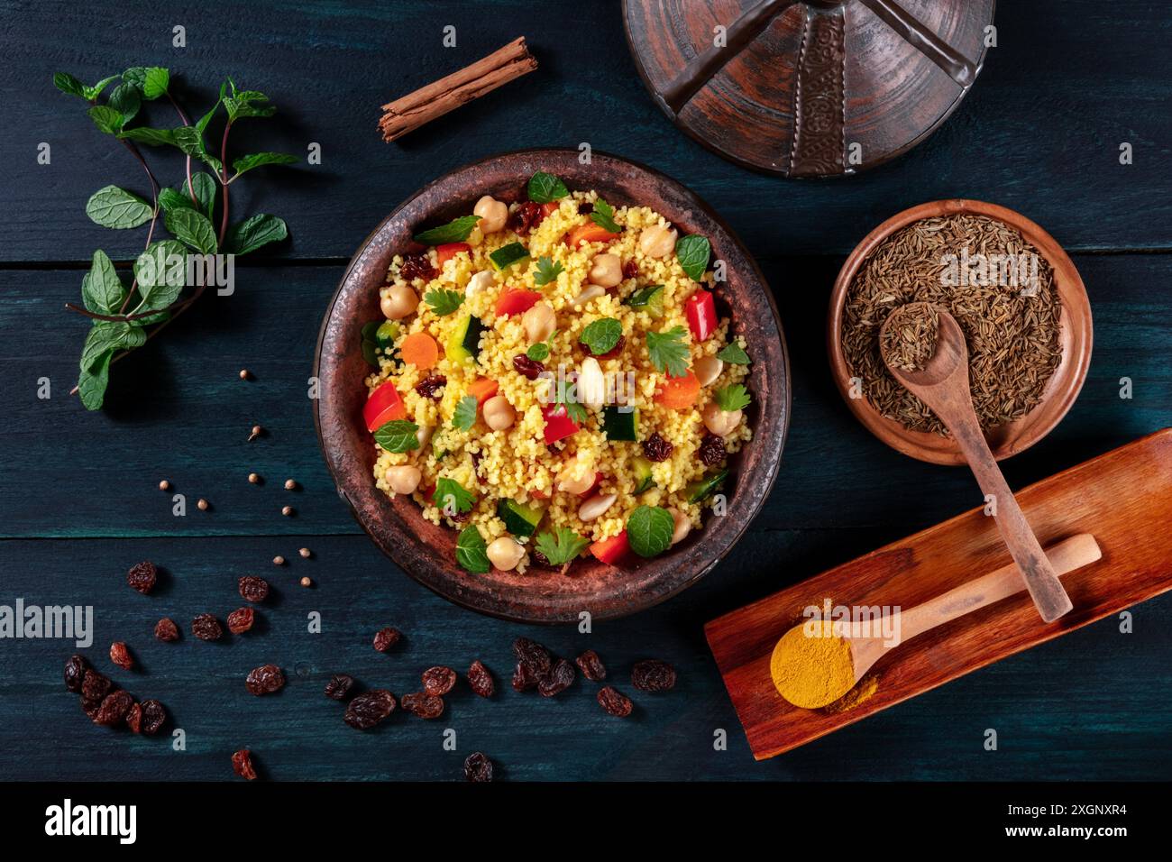 Traditioneller Couscous in einer Tajine, von oben mit Gewürzen und Kräutern auf dunklem Holzhintergrund geschossen Stockfoto