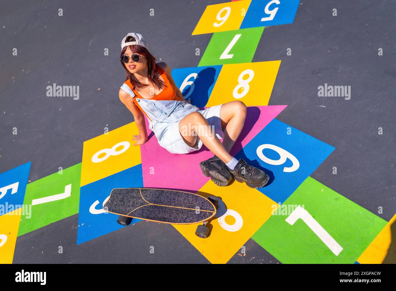 Coole junge chinesische Skaterin, die über einem farbenfrohen Bild von Street Art in einem urbanen Skateboard-Park sitzt Stockfoto