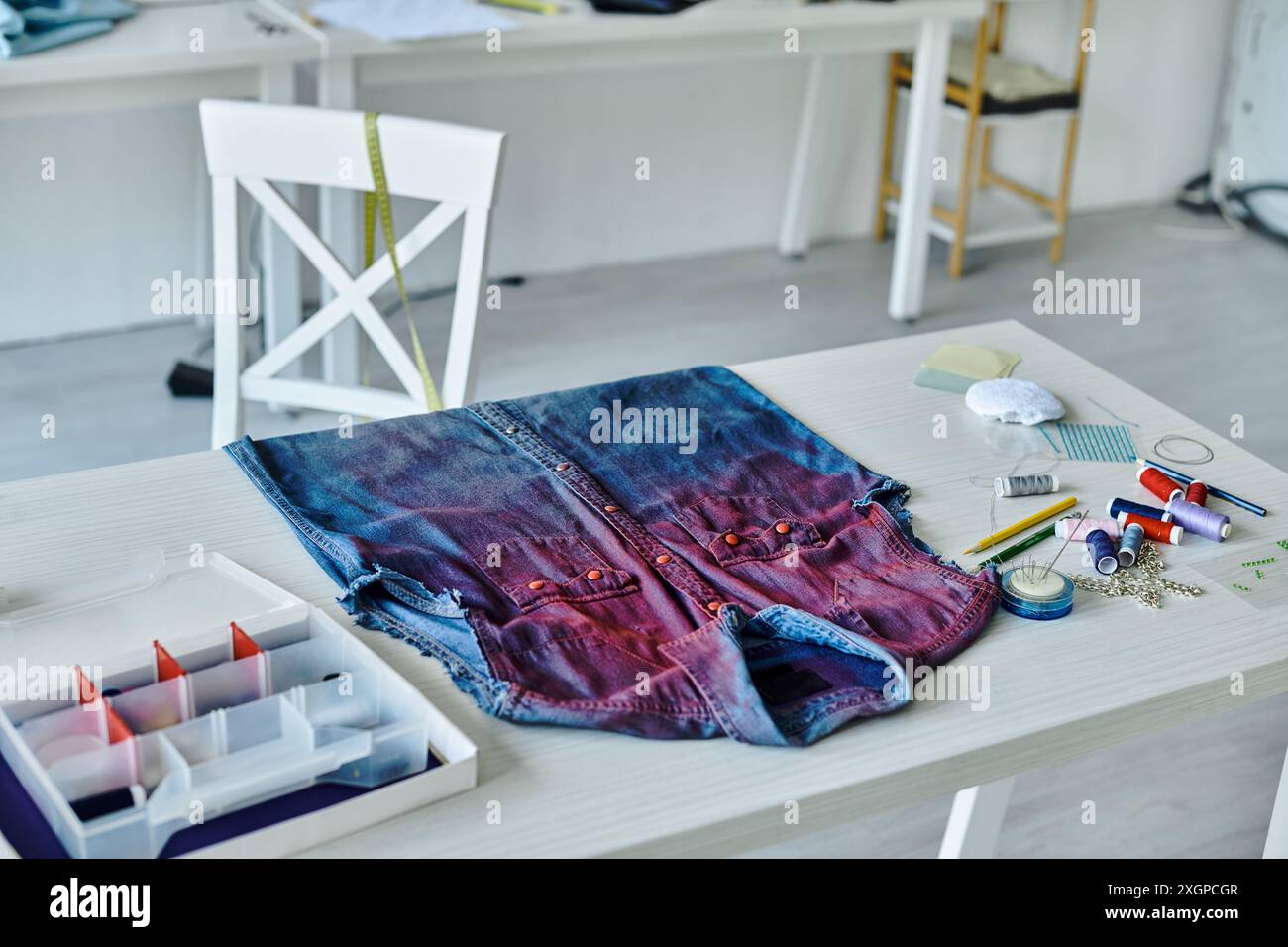 Eine Nahaufnahme eines Denim-Hemdes auf einem weißen Tisch mit Werkzeugen und Materialien zum Nähen und Restaurieren. Stockfoto