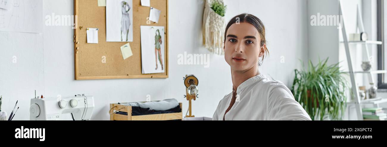 Ein junger Mann in einem weißen Hemd sitzt in seinem Atelier, umgeben von Werkzeugen seines Berufes, bereit, alte Kleidung neu zu beleben. Stockfoto