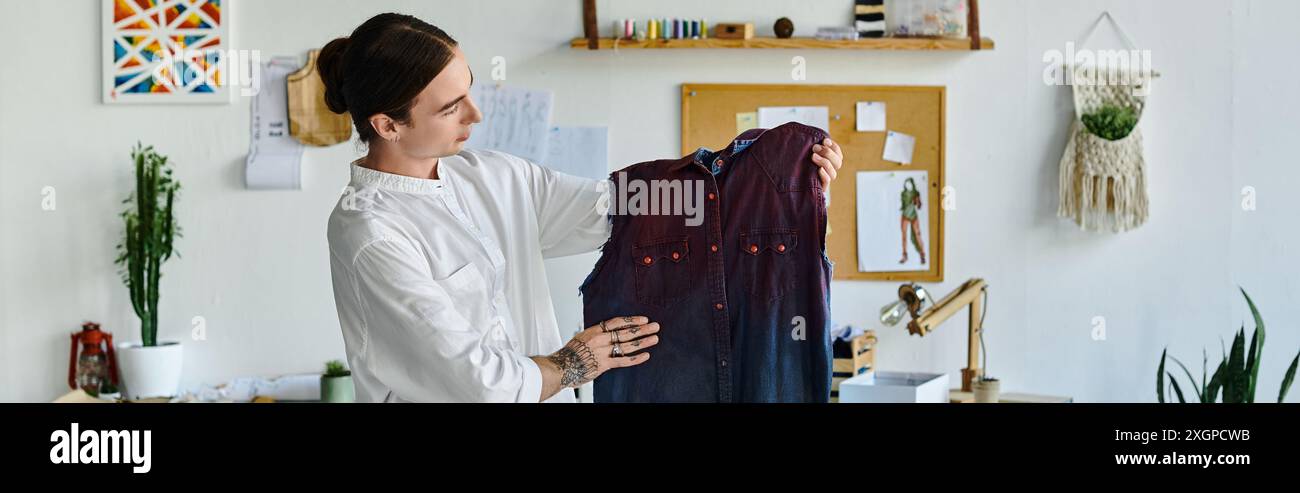 Ein junger Mann, der in einem weißen Hemd gekleidet ist, untersucht ein restauriertes Kleidungsstück in seinem Heimwerkeratelier und betont dabei nachhaltige Praktiken. Stockfoto