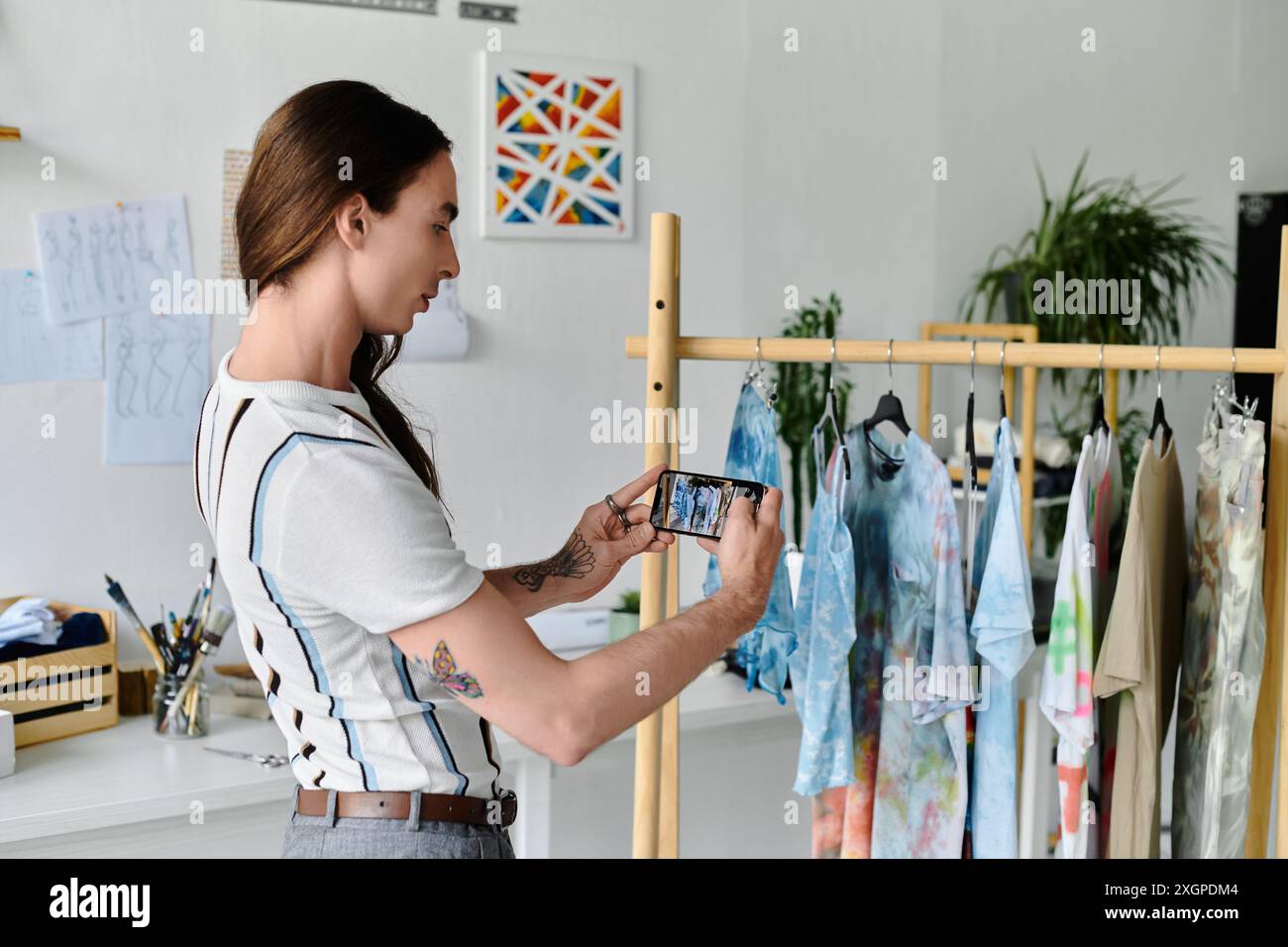 Ein junger Mann macht ein Foto seiner nachhaltigen Bekleidungskollektion und zeigt die lebendigen Farben und Muster. Stockfoto