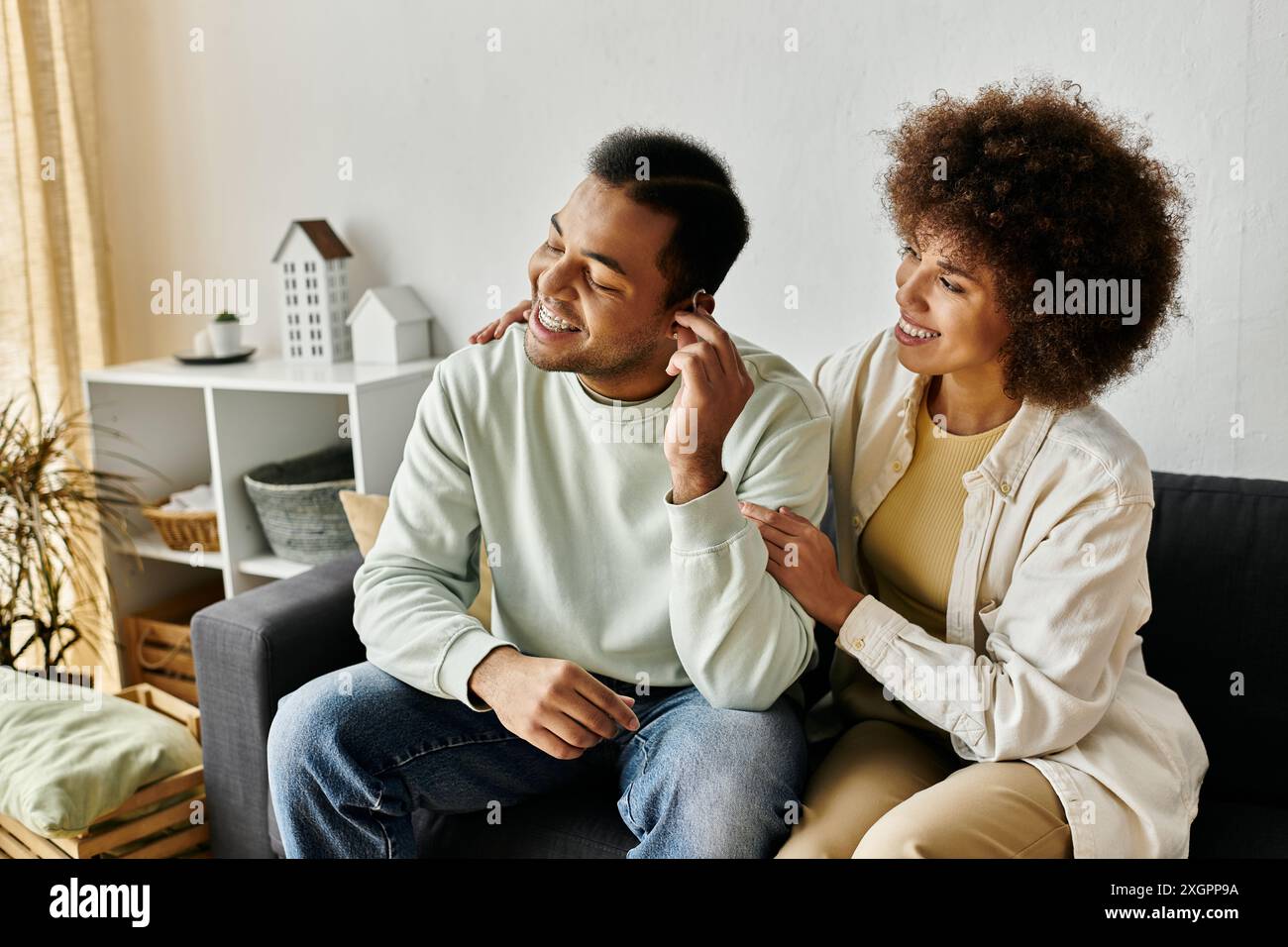 Gut aussehende afroamerikanische Frau, die ihrem Mann zu Hause mit Hörgerät hilft. Stockfoto