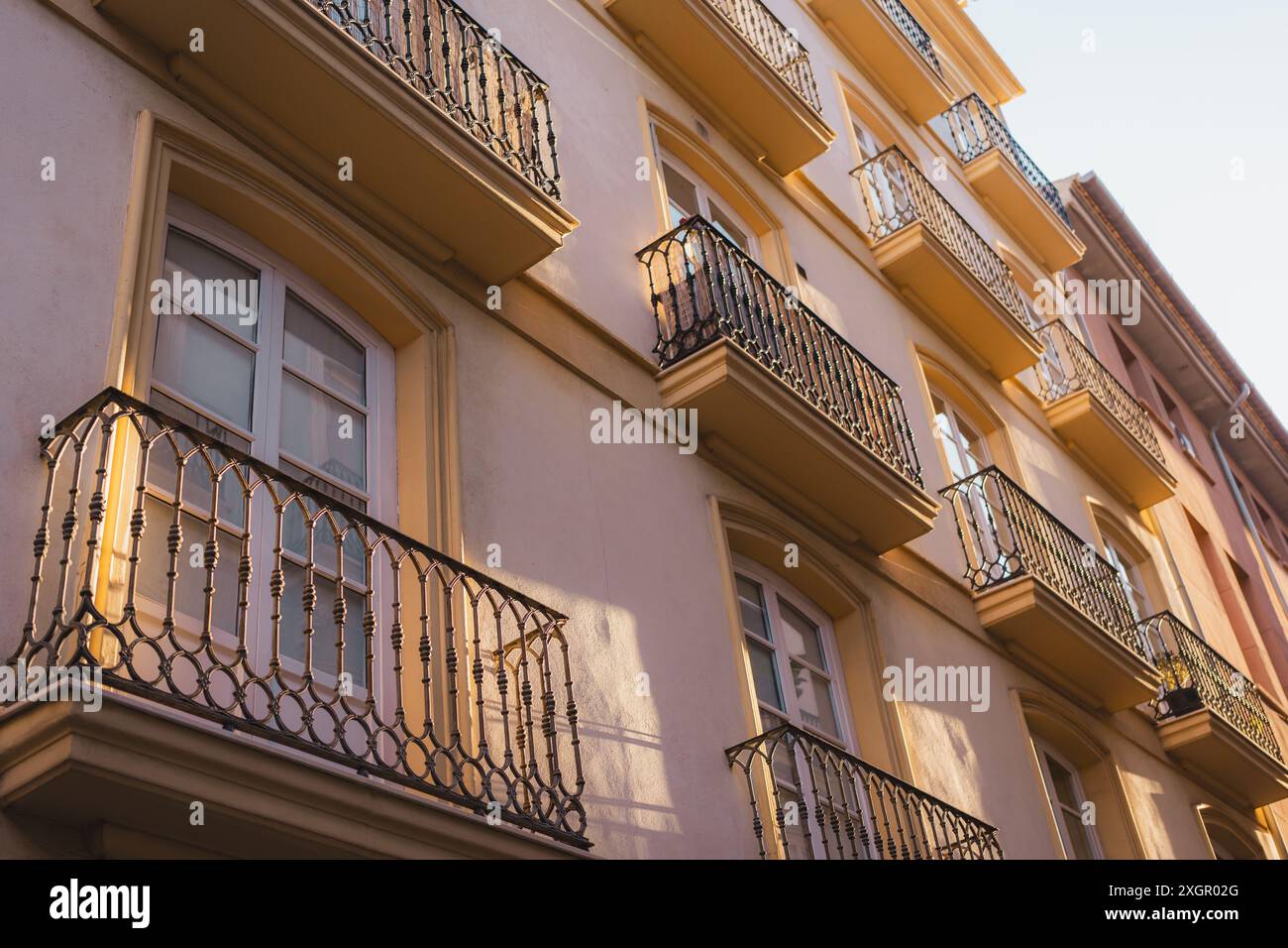 Eine Fassade eines Gebäudes mit mehreren Balkonen in Valencia, das in warmes Sonnenlicht getaucht ist. Die sich wiederholenden Muster und Schatten schaffen eine optisch ansprechende urbane Szene. Stockfoto