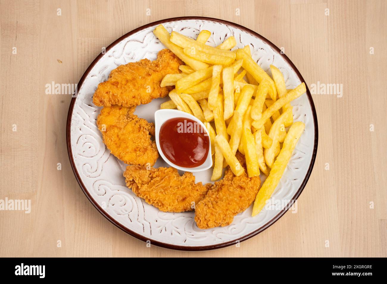 Ein Blick von oben auf einen Teller mit knusprigen gebratenen Hähnchenflügeln mit Pommes frites und einer Seite Ketchup auf einem Holztisch Stockfoto