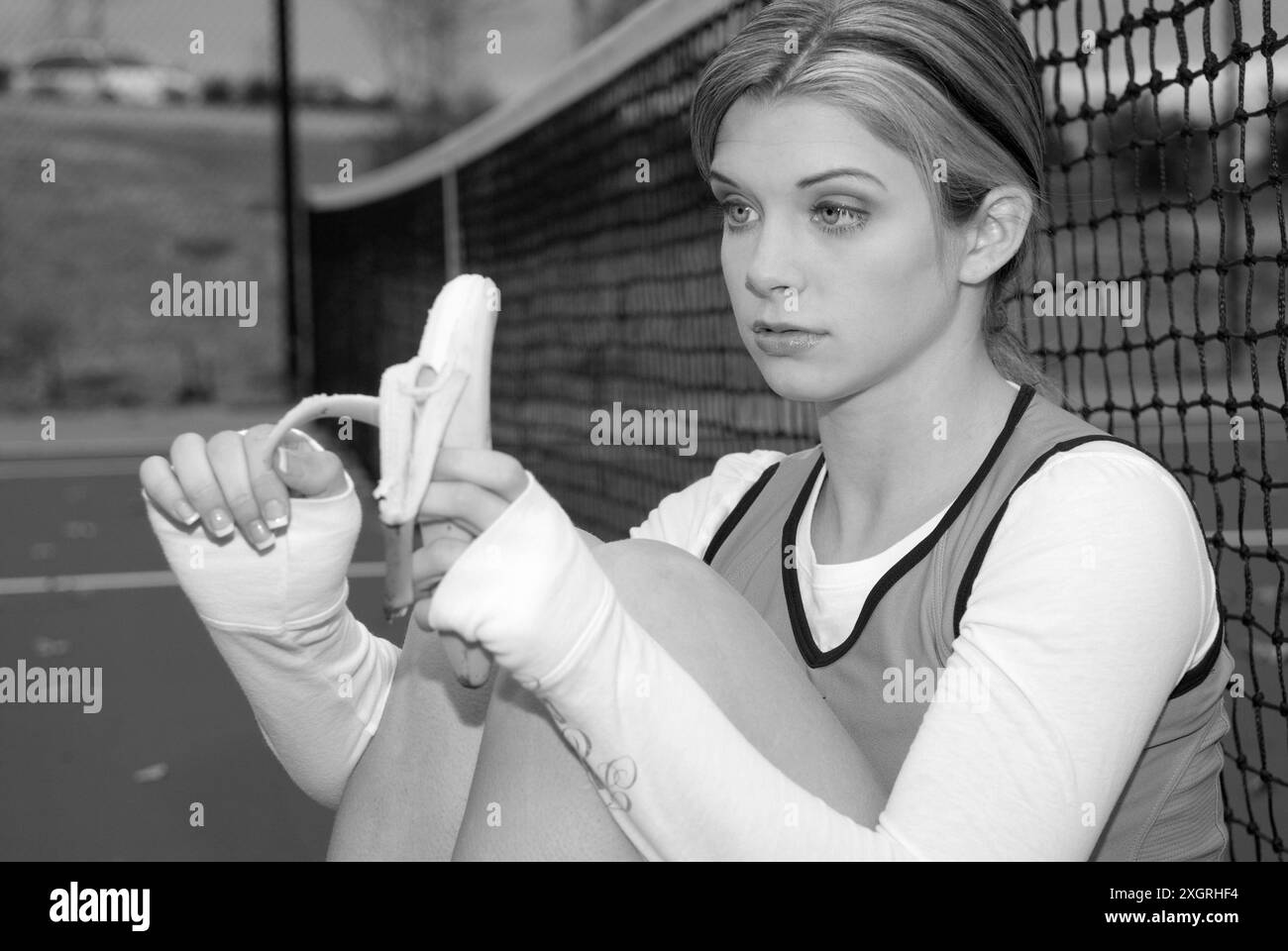 Kaukasisches Teenager-Mädchen von 15 bis 17 Jahren, die eine Pause vom Tennisspielen macht, um eine Banane zu essen. USA Stockfoto