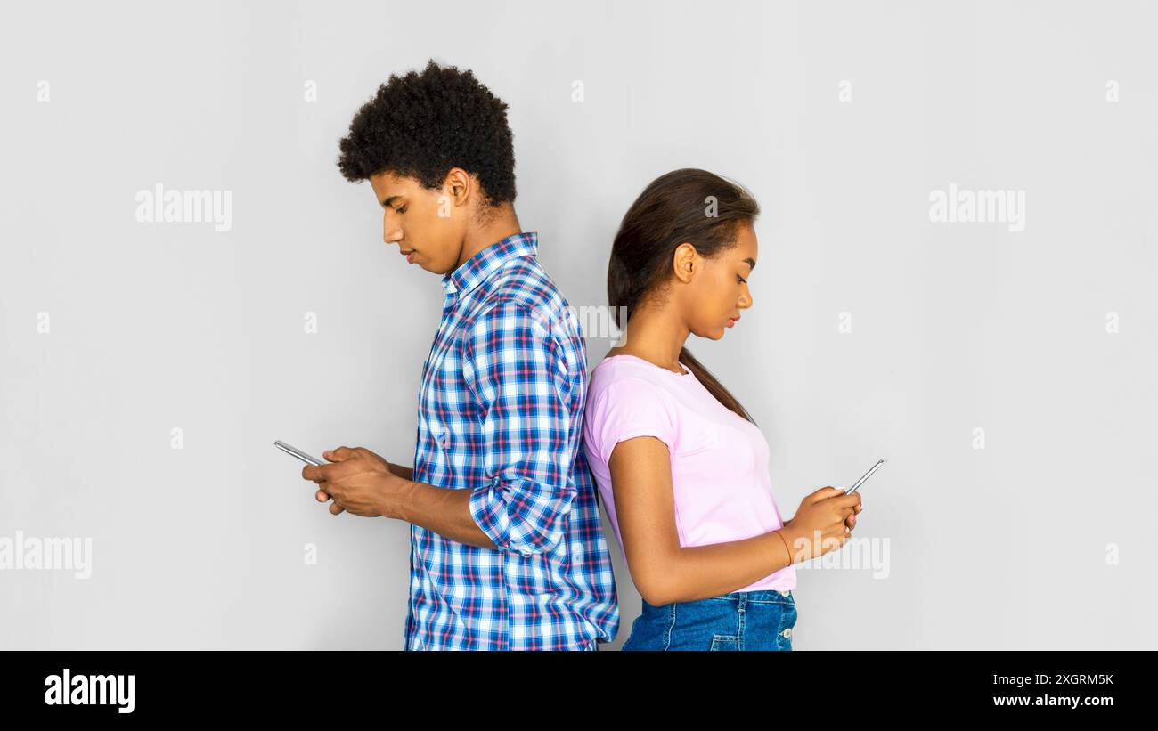 Teenager-Paar, Das Smartphones Gegen Grey Wall Benutzt Stockfoto