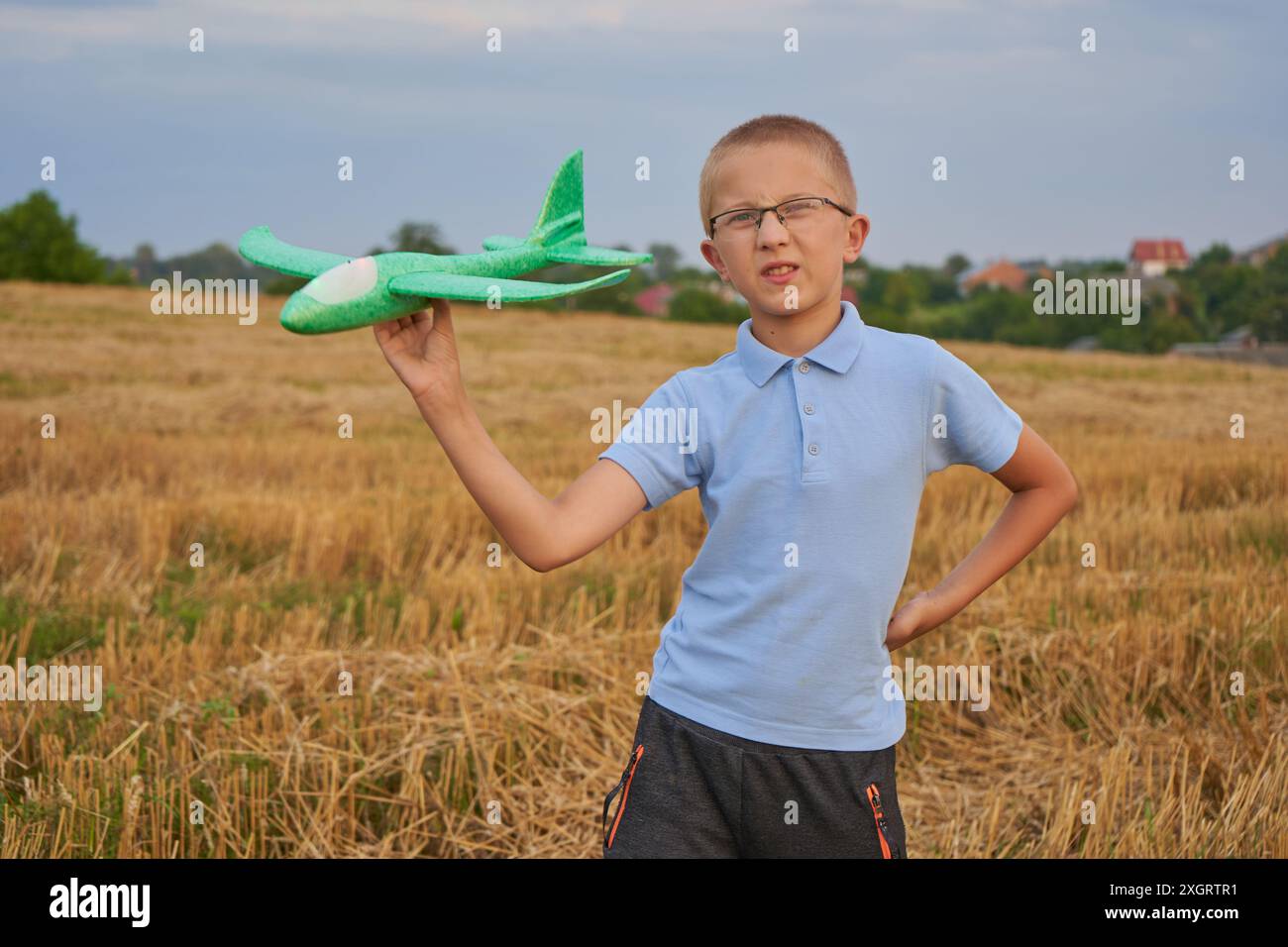 Ein Junge in Brille hält und spielt mit einem Flugzeug auf einem Weizenfeld Stockfoto