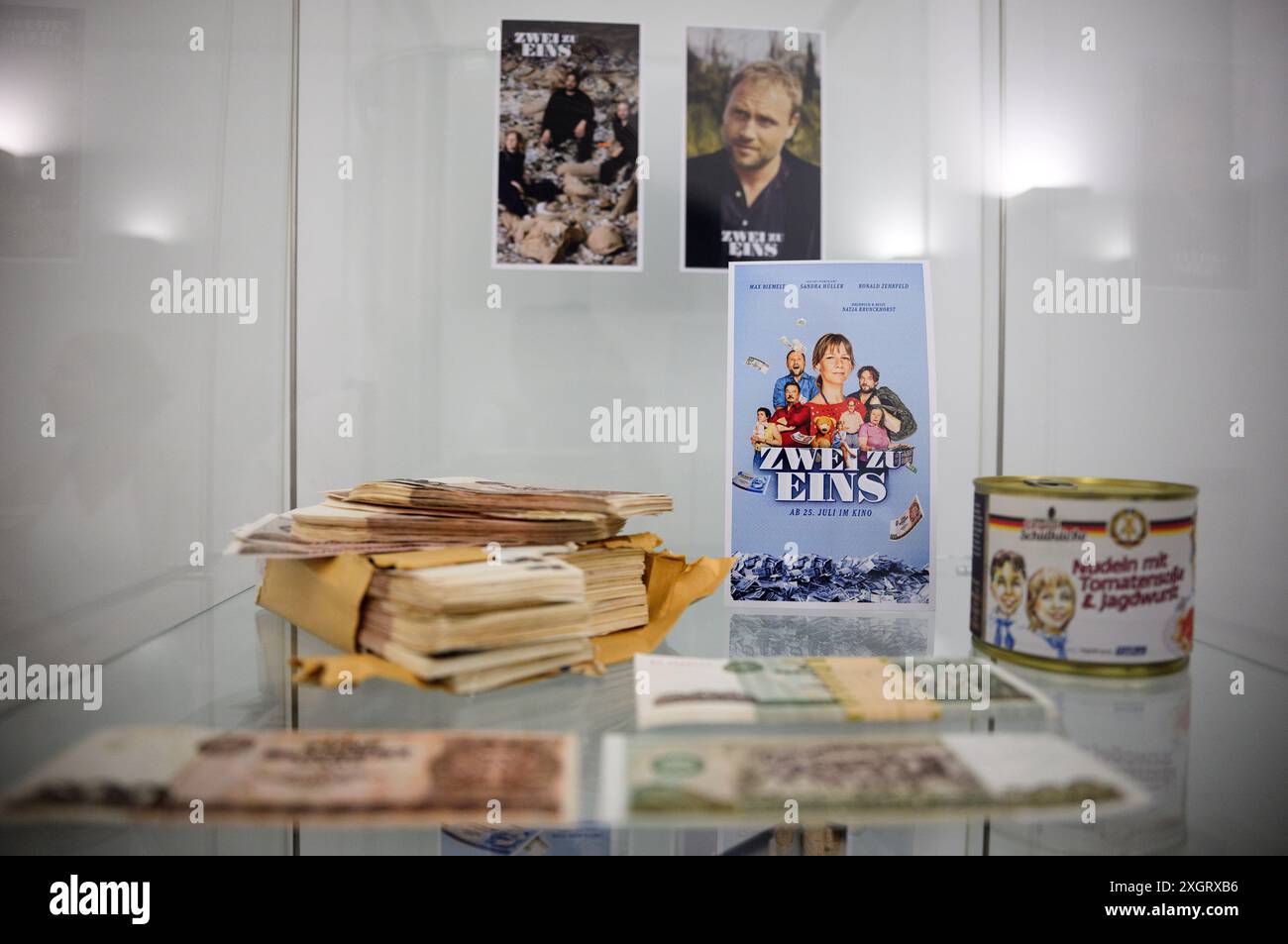 PRODUKTION - 10. Juli 2024, Berlin: DDR-Mark-Bündel und ein Verweis auf den Film „zwei zu eins“ liegen in einer Vitrine in der Berliner Filiale der Kreditanstalt für Wiederaufbau (KfW). Im Frühjahr 1990 begann die DDR-Landesbank, das ostdeutsche Papiergeld in einem alten Tunnel in Halberstadt (Sachsen-Anhalt) hinter dicken Betonmauern zu lagern, wo es verrotten sollte. Seit der währungsunion am 1. Juli 1990 wurde die D-Mark auch als Zahlungsmittel im Osten genutzt, die Ost-Mark war kurz darauf wertlos. 11 Jahre später war der Tunnel jedoch noch b Stockfoto