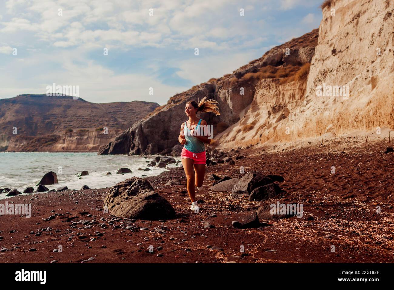 Junge Frau, die auf dem Meer am Roten Strand auf Santorin läuft. Läuferinnen joggen während des Workouts im Freien und genießen den Blick auf die Meereslandschaft. Gesundes sportiv Stockfoto